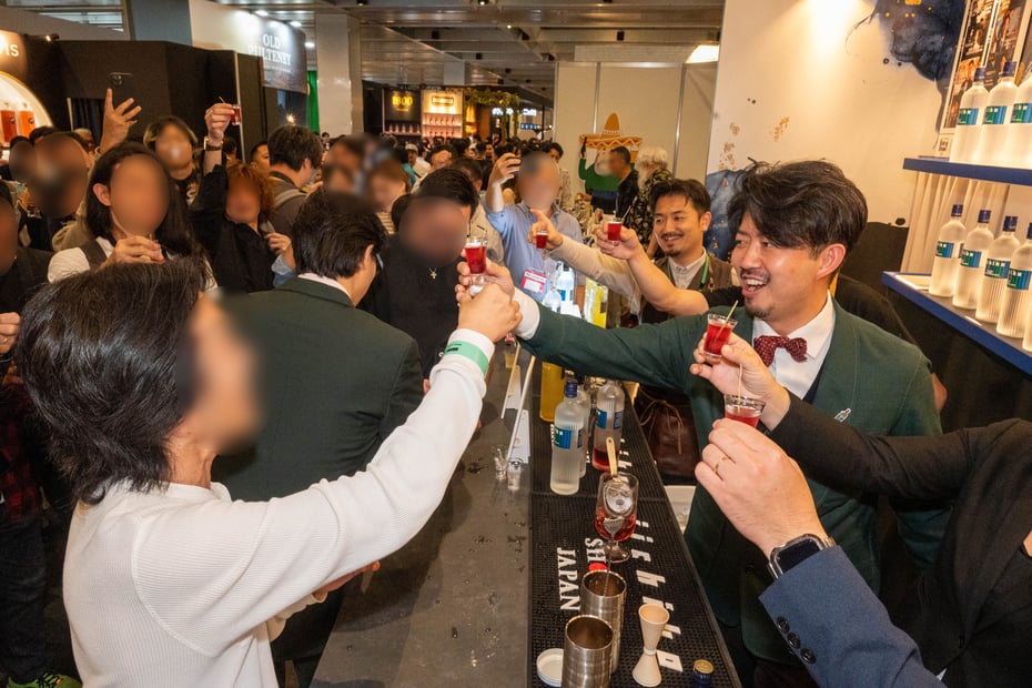 訪れたお客様と乾杯をするバーテンダー。笑顔が溢れる三和酒類のブースの様子。